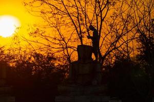 Silhouette Buddha statue and Asian worker, he is working and casting Buddha statue at twilight sunset background. Thailand. photo