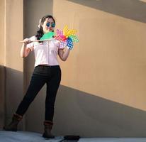 una mujer asiática publica y juega un juguete de molino de viento con el colorido arco iris en la azotea del edificio al atardecer. foto