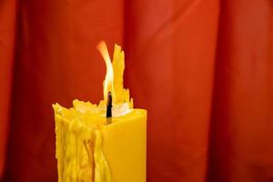 Close up to the melt yellow candle and fire flame with the red curtain background. photo