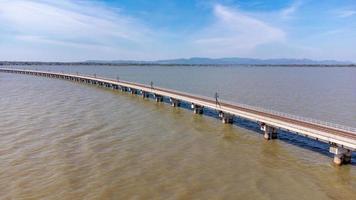 Aerial view of an amazing travel train parked on a floating railway bridge over the water of the lake in Pa Sak Jolasid dam with blue sky at Lopburi, Thailand. photo