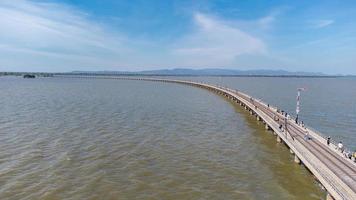 Aerial view of an amazing travel train parked on a floating railway bridge over the water of the lake in Pa Sak Jolasid dam with blue sky at Lopburi, Thailand. photo