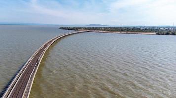 Aerial view of an amazing travel train parked on a floating railway bridge over the water of the lake in Pa Sak Jolasid dam with blue sky at Lopburi, Thailand. photo