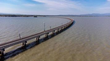 Aerial view of an amazing travel train parked on a floating railway bridge over the water of the lake in Pa Sak Jolasid dam with blue sky at Lopburi, Thailand. photo