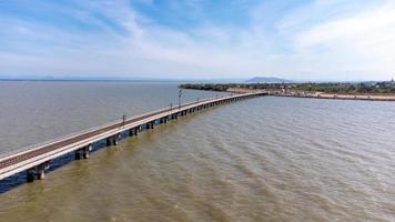 Aerial view of an amazing travel train parked on a floating railway bridge over the water of the lake in Pa Sak Jolasid dam with blue sky at Lopburi, Thailand. photo