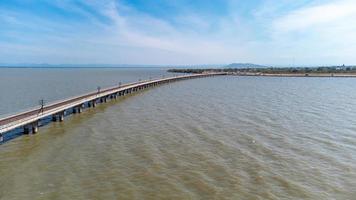 Aerial view of an amazing travel train parked on a floating railway bridge over the water of the lake in Pa Sak Jolasid dam with blue sky at Lopburi, Thailand. photo