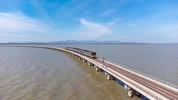 Aerial view of an amazing travel train parked on a floating railway bridge over the water of the lake in Pa Sak Jolasid dam with blue sky at Lopburi, Thailand. photo