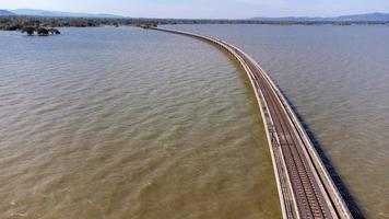 Aerial view of an amazing travel train parked on a floating railway bridge over the water of the lake in Pa Sak Jolasid dam with blue sky at Lopburi, Thailand. photo