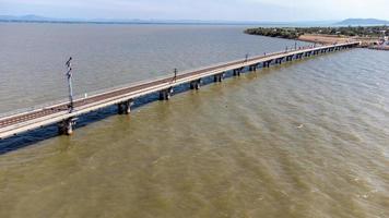 Aerial view of an amazing travel train parked on a floating railway bridge over the water of the lake in Pa Sak Jolasid dam with blue sky at Lopburi, Thailand. photo