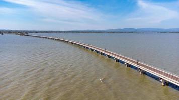 Aerial view of an amazing travel train parked on a floating railway bridge over the water of the lake in Pa Sak Jolasid dam with blue sky at Lopburi, Thailand. photo