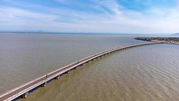 Aerial view of an amazing travel train parked on a floating railway bridge over the water of the lake in Pa Sak Jolasid dam with blue sky at Lopburi, Thailand. photo