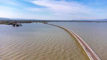 vista aérea de un increíble tren de viaje estacionado en un puente ferroviario flotante sobre el agua del lago en la presa pa sak jolasid con cielo azul en lopburi, tailandia. foto