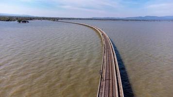 Aerial view of an amazing travel train parked on a floating railway bridge over the water of the lake in Pa Sak Jolasid dam with blue sky at Lopburi, Thailand. photo