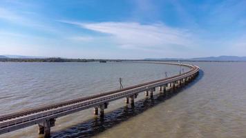 Aerial view of an amazing travel train parked on a floating railway bridge over the water of the lake in Pa Sak Jolasid dam with blue sky at Lopburi, Thailand. photo