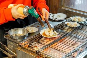 Hand of chef using burner cooking and burn big scallops shells with cheese on stove to sale for customer at Kuromon market. scallops Bar-B-Q is popular among tourists who come to the Osaka, Japan. photo