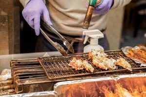 mano del chef usando quemadores para cocinar y quemar patas de cangrejo real en la estufa para venderlas al cliente en el mercado de kuromon. El bar-bq de patas de cangrejo real es popular entre los turistas que vienen de viaje a osaka, japón. foto