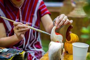 cierre y recorte las manos de una niña sosteniendo un estudio de pincel y aprendiendo pintura sobre una muñeca de madera en el aula de arte de su escuela. foto