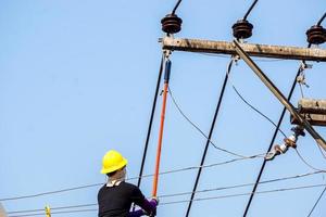 electricistas de primer plano y cultivos que trabajan en el teleférico para reparar la línea eléctrica bajo un fondo de cielo azul claro. foto