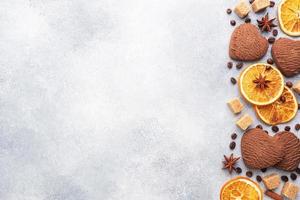 galletas de corazón de chocolate, naranjas, canela y especias picantes en una mesa gris, vista superior, espacio para copiar. foto