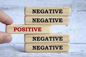 Negative and positive text on wooden blocks with hand placing a wooden block in the middle. photo