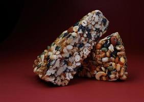 Two pieces of gozinak from various nuts with dried fruits on a red background. photo