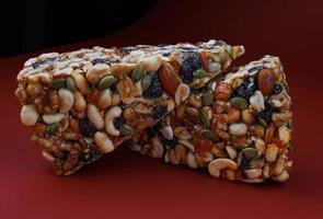 Two pieces of gozinak from various nuts with dried fruits on a red background. photo