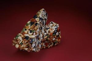 Two pieces of gozinak from various nuts with dried fruits on a red background. photo