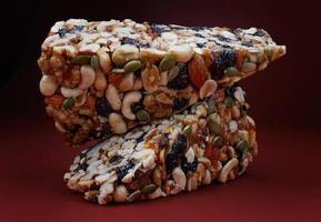 Two pieces of gozinak from various nuts with dried fruits on a red background. photo