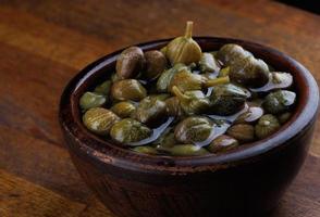 A bowl of pickled capers stands on a wooden surface. photo