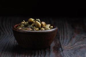 Capers in a clay cup standing on a wooden table. photo