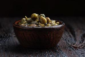 Pickled capers in brine. Clay cup full of capers. photo