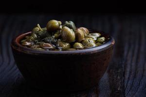 An earthenware bowl filled to the brim with capers stands on a wooden table. photo