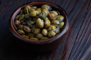 An earthenware bowl filled to the brim with capers stands on a wooden table. photo