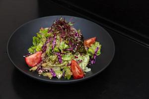 salad in a black plate, on a black wooden background photo