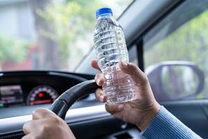 Asian woman driver holding bottle for drink water while driving a car. Plastic hot water bottle cause fire. photo