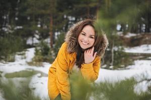 Portrait of young smiling beautiful woman in yellow jacket walking in the winter forest photo