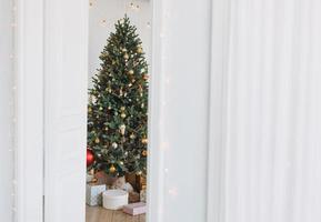 Decorated Christmas tree in golden and white toys with the gift boxes from door at the bright interior, textured background photo