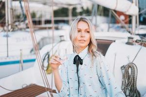 bella joven rubia vestida de azul con un vaso de soda en un barco en el muelle al atardecer foto