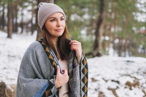 retrato de joven morena hermosa mujer con sombrero y poncho gris en el bosque de invierno foto