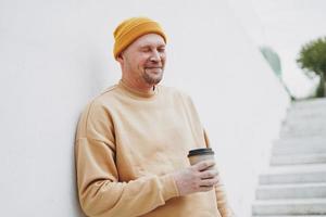 Portrait of stylish man hipster in yellow hat with paper cup of coffee at the city photo