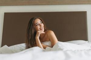 hermosa joven asiática con el pelo largo en la cama con ropa de cama blanca de la habitación del hotel foto