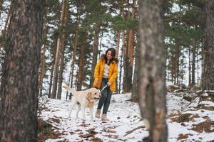 Young smiling woman in yellow jacket with big kind white dog Labrador walking in winter forest photo