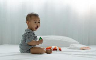 bebé asiático jugando juguetes y rompecabezas de madera en la cama. el bebé está feliz de estar juntos. actividades para promover el desarrollo de la edad del bebé. foto