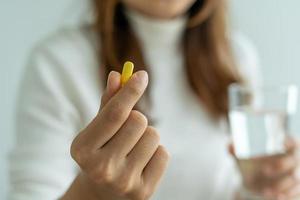 Close up of hand's woman holding a dietary supplement or medication or vitamin and a glass of water ready to take. healthcare, medicine,Self-care,Illness and pharmacy concept.