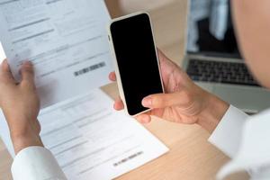un hombre de negocios usa su teléfono para escanear un código de barras para pagar la factura mensual de su tarjeta de crédito después de recibir una factura. concepto de pago de facturas en línea foto