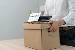 A businessman holds a box for personal items after sending a resignation letter to an executive or boss. Include information about resignation and vacancies and job changes. photo