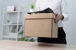 A businessman holds a box for personal items after sending a resignation letter to an executive or boss. Include information about resignation and vacancies and job changes. photo