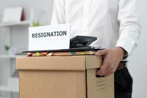 A businessman holds a box for personal items after sending a resignation letter to an executive or boss. Include information about resignation and vacancies and job changes. photo