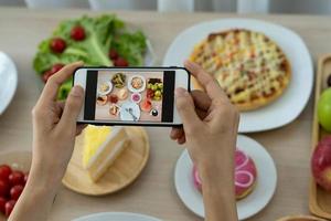 A reviewer's hand using a mobile phone to take pictures of food at a restaurant table.Take photo to write a review of the restaurant to share on the internet.