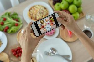 las mujeres usan teléfonos móviles para tomar fotografías de alimentos o grabar videos en vivo en aplicaciones de redes sociales. la comida para la cena se ve apetitosa. fotografiar y tomar una foto para revisar los conceptos de comida