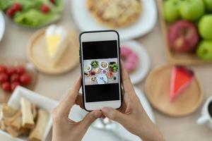 las mujeres usan teléfonos móviles para tomar fotografías de alimentos o grabar videos en vivo en aplicaciones de redes sociales. la comida para la cena se ve apetitosa. fotografiar y tomar una foto para revisar los conceptos de comida